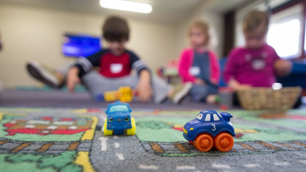 Toy cars on a play mat in a daycare with children playing in the background