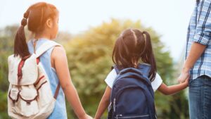 Father walking daughters to school wearing backpacks and holding hands