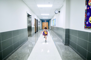 Child skipping down hallway of school wearing book bag