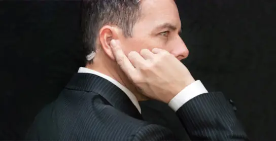 Private security officer using his finger to listen to device in his ear.
